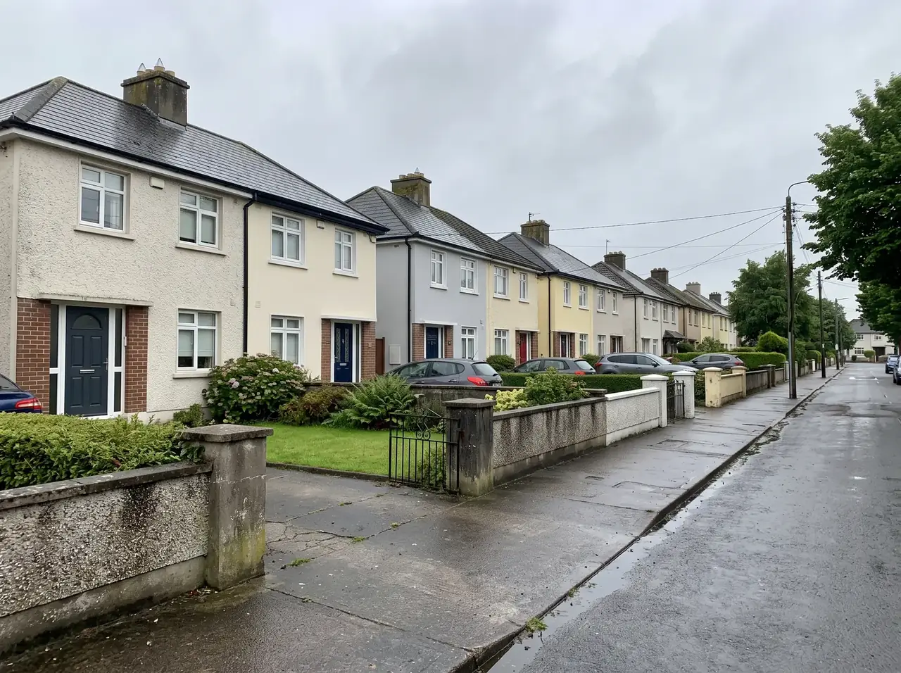 Row of semi-detached houses with painted render and low garden walls on a wet suburban street
