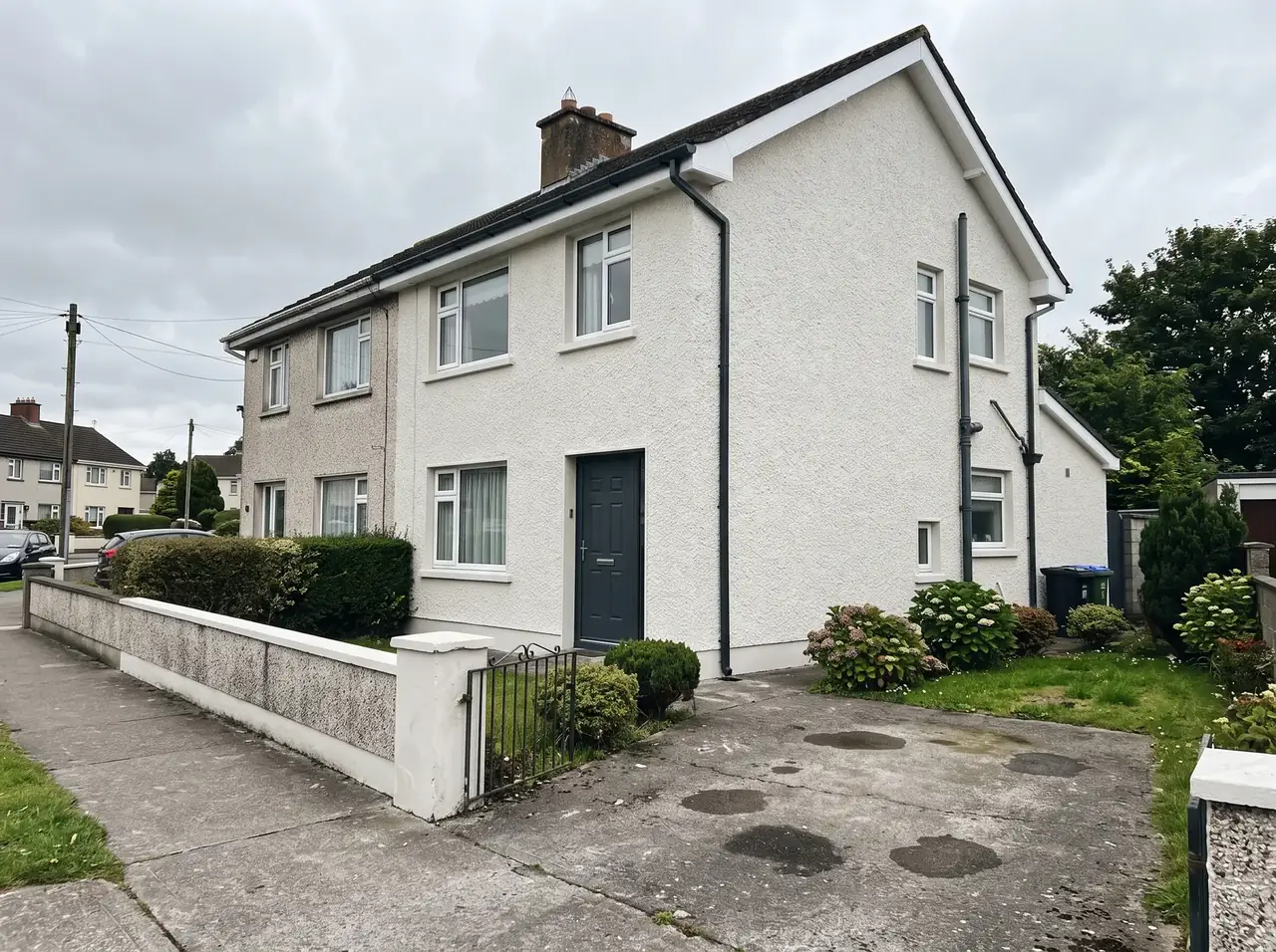 Semi-detached house with freshly painted off-white render, dark grey front door and white fascia