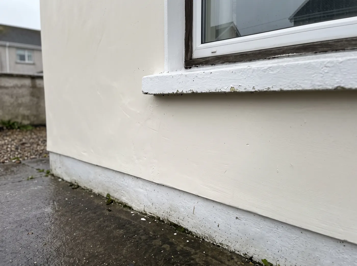 Window sill with flaking paint and scuffed render beside it, the kind of surface that is scraped, filled and primed before repainting