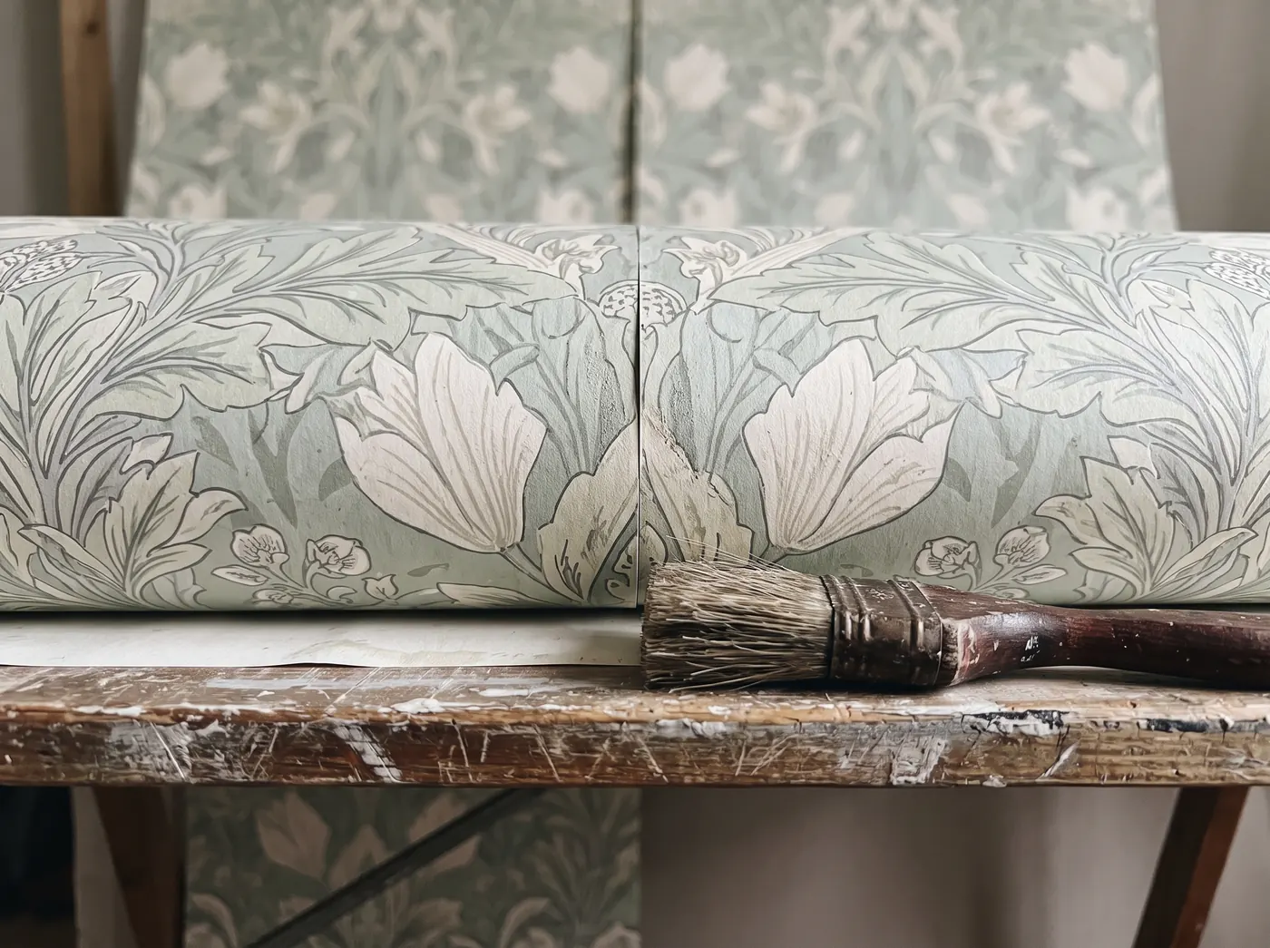 Two lengths of patterned wallpaper on a pasting table with the pattern lined up at the join, and a paste brush beside them
